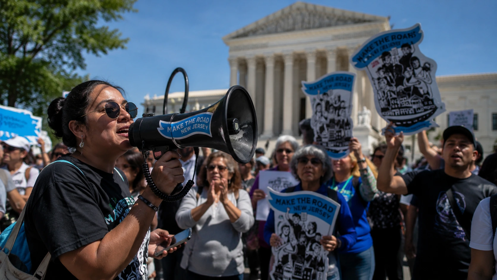 A crowd of immigration advocates holds signs and listens to a speaker with a megaphone outside the U.S. Supreme Court during a rally supporting birthright citizenship.